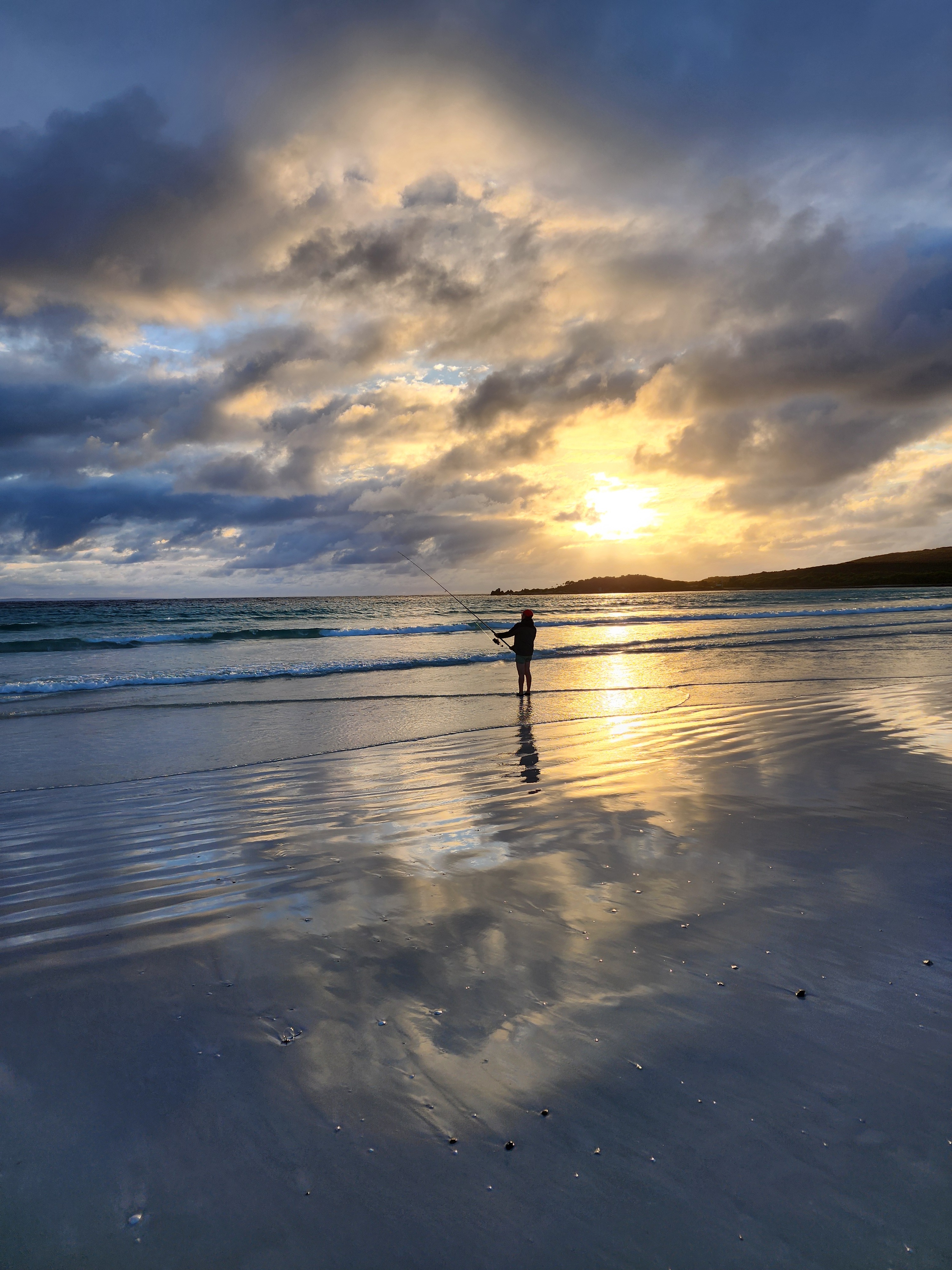 Fisherman stands on the beach fishing at sunrise
