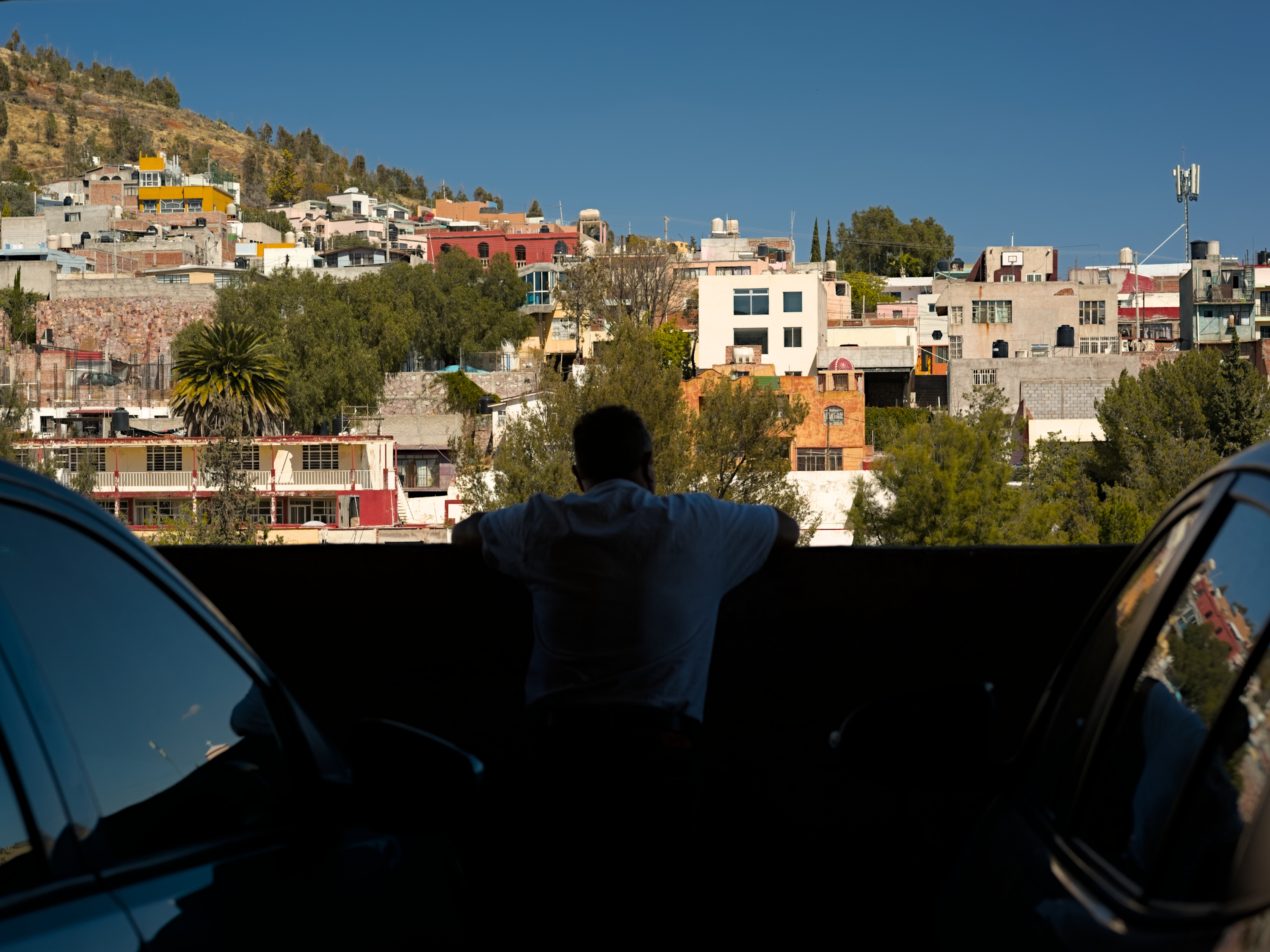 A man standing against a wall resting his arms under the shadow of the parking garage looking at the view of the city