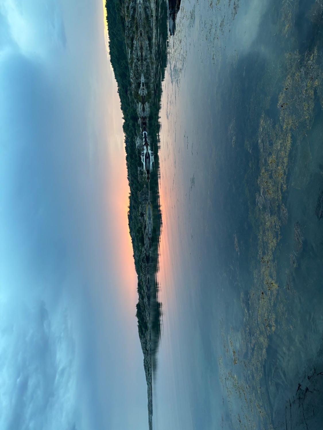 A small dark strip of land out in the sea, turned 90 degrees. A faint red light from the setting sun. 