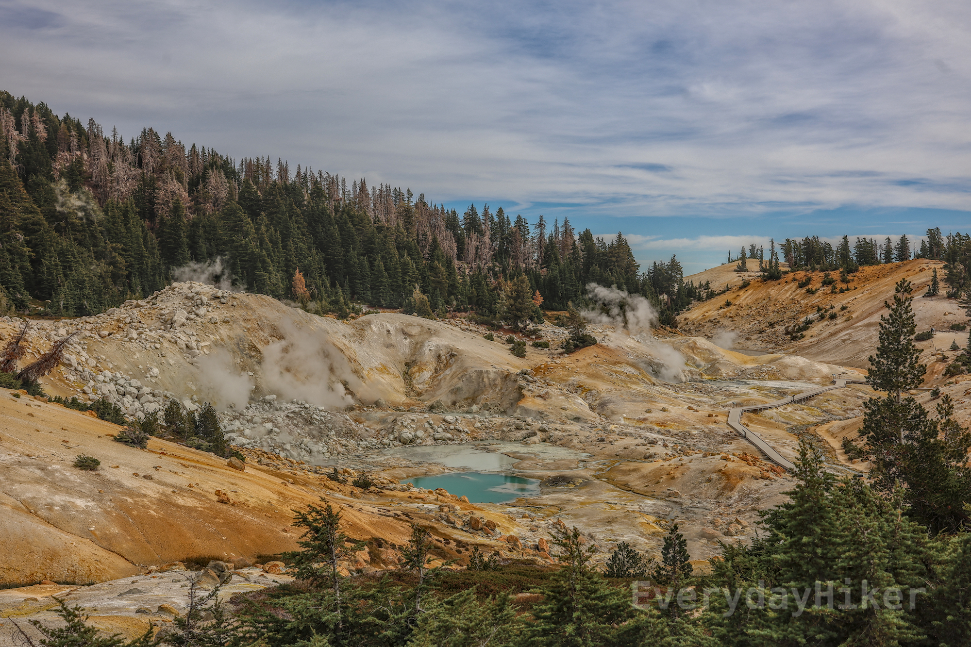 Various pools of turquoise or grey water with steam escaping from hydrothermal vents make up Bumpass Hell, an inhospitable landscape with the slight screaming sounds emanating all around it.  A boardwalk cuts along the pools for viewing up close.  Outside of the 'hell', evergreens grow in the corners of the frame.